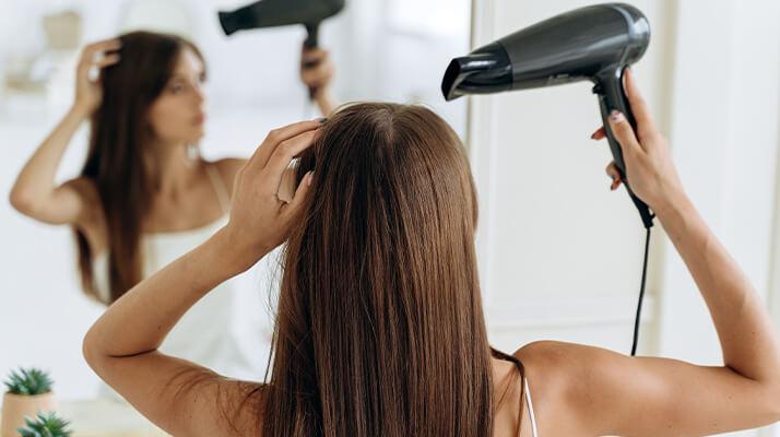 une femme aux cheveux longs utilise un sèche-cheveux