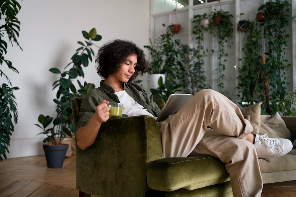 Une jeune femme assise sur un fauteuil lisant un livre et tenant une tasse